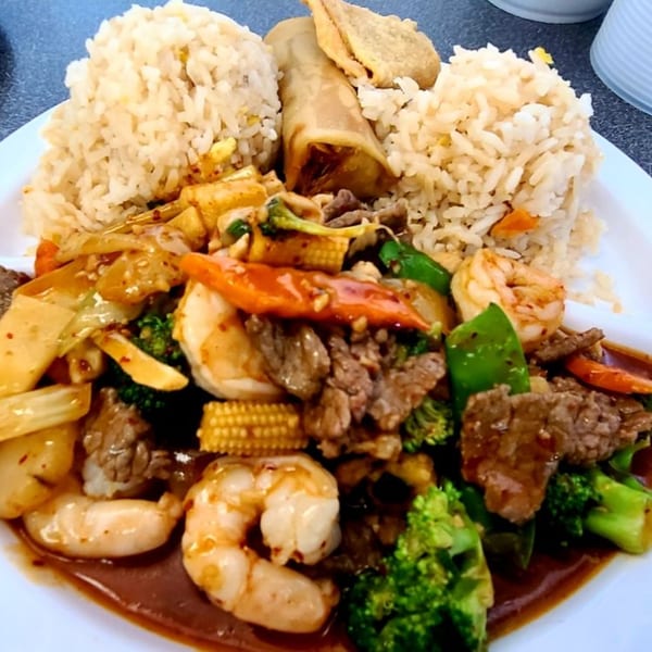 A Chinese fast food combo plate with fried rice, egg roll, beef, shrimp, and mixed vegetables.